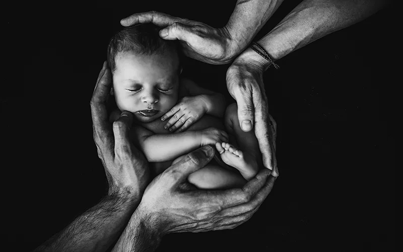 Foto de um bebê envolto nas mãos da mãe e do pai.