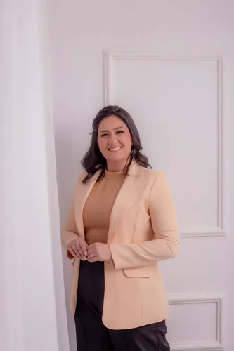 Na foto uma mulher com blazer bege, cabelo preto e sorrindo.