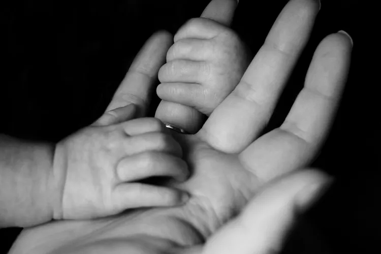 Mãos do bebê entrelaçadas às mãos de um adulto