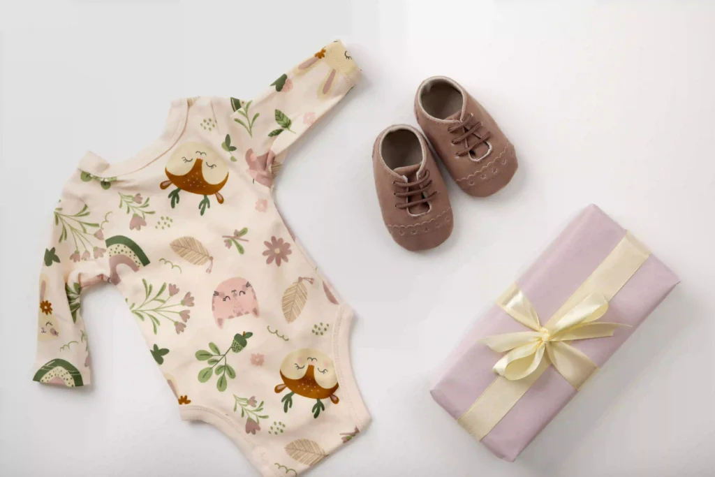 Imagem com um body de bebê rrecém-nascido estampado, com sapatos de bebê marrom e um pacote de presente com. laço amarelo.