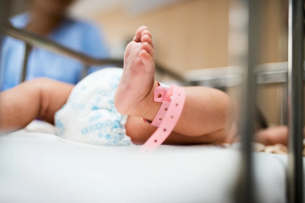Pé de criança recém-nascida com pulseira rosa da maternidade.