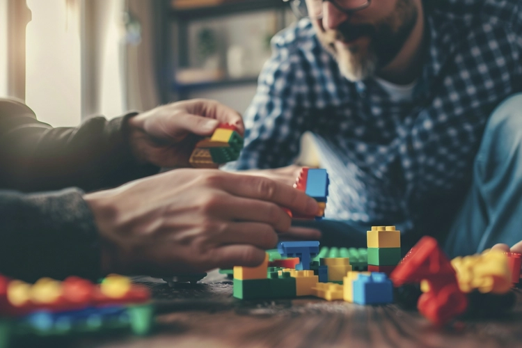 Duas pessoas montam blocos de brinquedo coloridos juntas sobre uma mesa de madeira, em um ambiente aconchegante, simbolizando cooperação e criatividade.