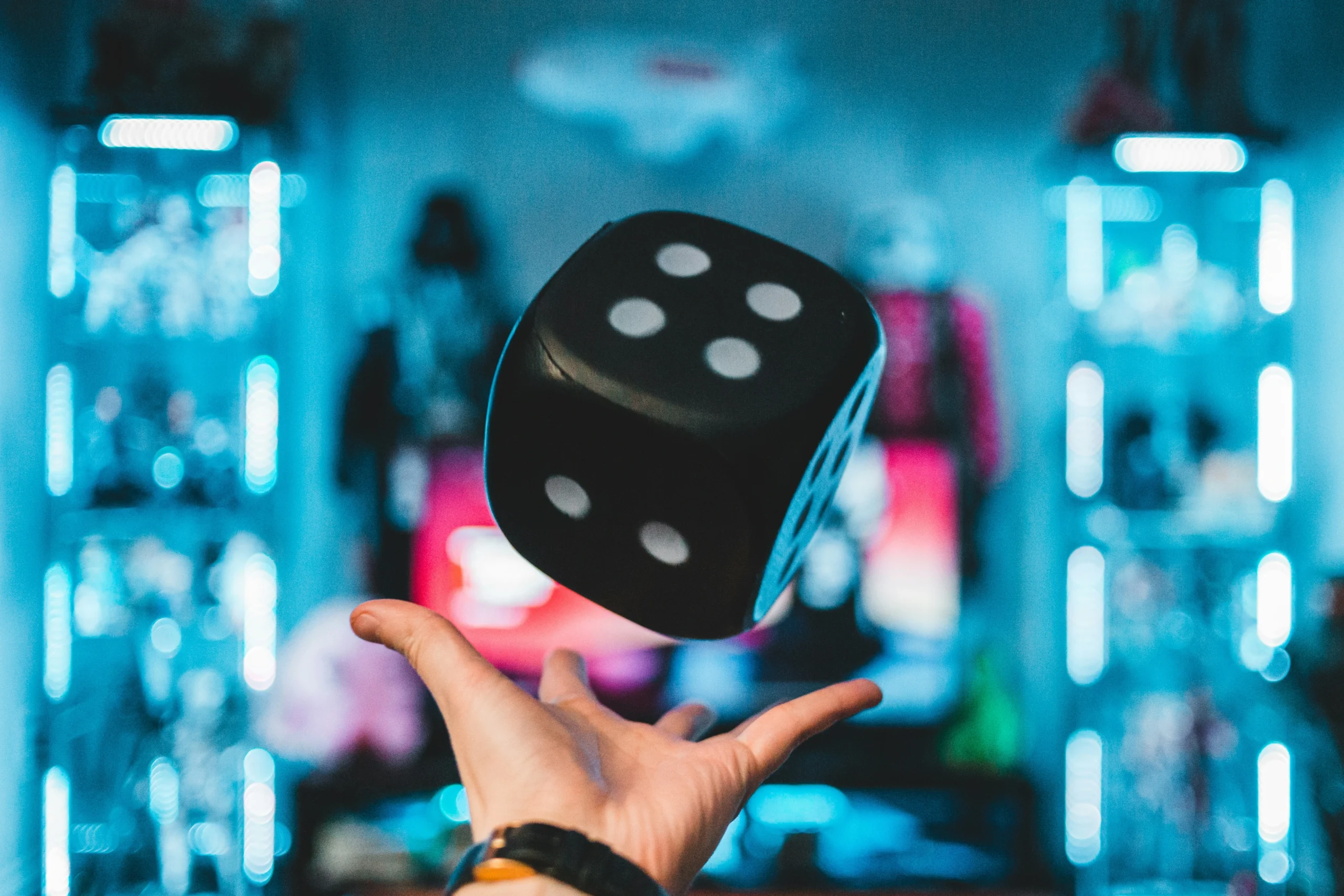 Fundo com luzes em neón azul e branco e em detaque uma mão branca de um menino joga um dado preto de um jogo de tabuleiro no ar.