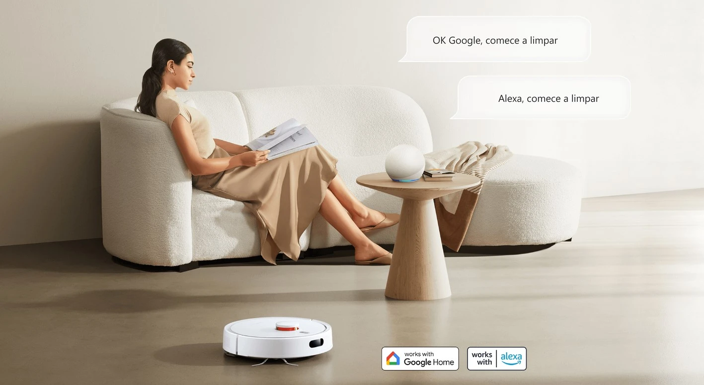 Mulher sentada em um sofá moderno, lendo uma revista, enquanto um aspirador de pó inteligente S20 limpa o chão automaticamente. Ao lado dela, há uma mesa com um dispositivo inteligente compatível com Google Home e Alexa, com comandos de voz na tela dizendo: “OK Google, comece a limpar” e “Alexa, comece a limpar”. O ambiente é minimalista e acolhedor, com tons neutros e decoração suave.