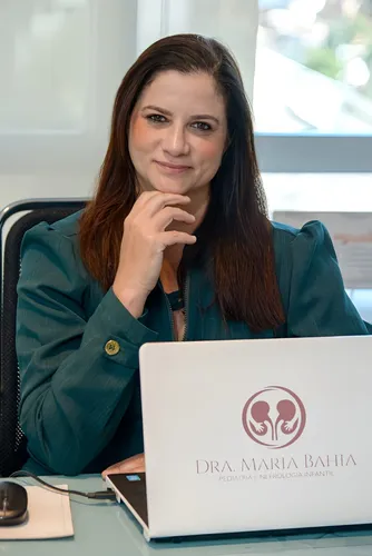 Mulher vestida de verde com a mão no queixo, sentada em frente a um notebook.
