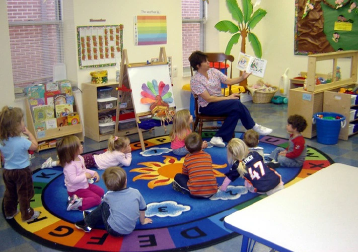 Professora lê para crianças sentadas em círculo em uma sala de aula colorida.