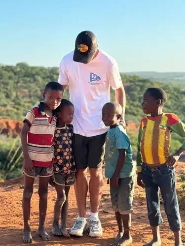 adolescente branco de boné e camiseta branca abraça crianças africanas que aparecem sorrindo