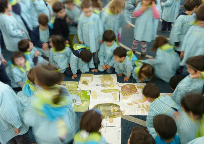 grupo de alunos vestindo uniforme azul se reúnem ao redor de imagens postas no chão