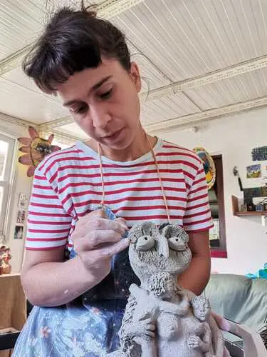 mulher branca vestida com camiseta branca e listras vermelhas aparece de frente mexendo em escultura