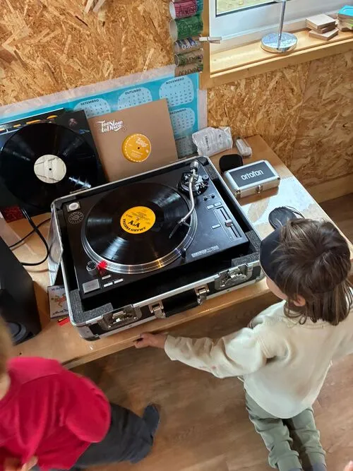 duas crianças, uma vestida de camiseta branca e outra de blusa vermelha, aparecem de costas olhando para instrumento musical e vinil